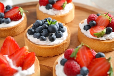 Photo of Wooden plate with different berry tarts. Delicious pastries