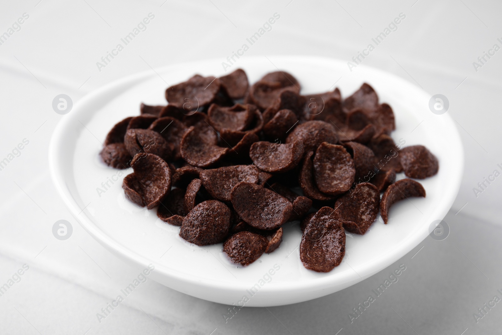 Photo of Breakfast cereal. Chocolate corn flakes and milk in bowl on white tiled table, closeup