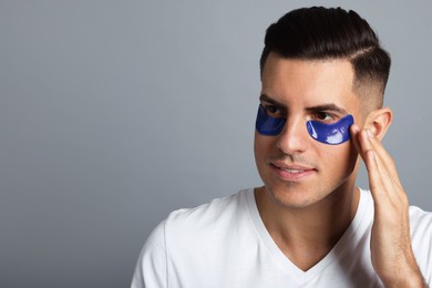 Man applying blue under eye patch on grey background. Space for text