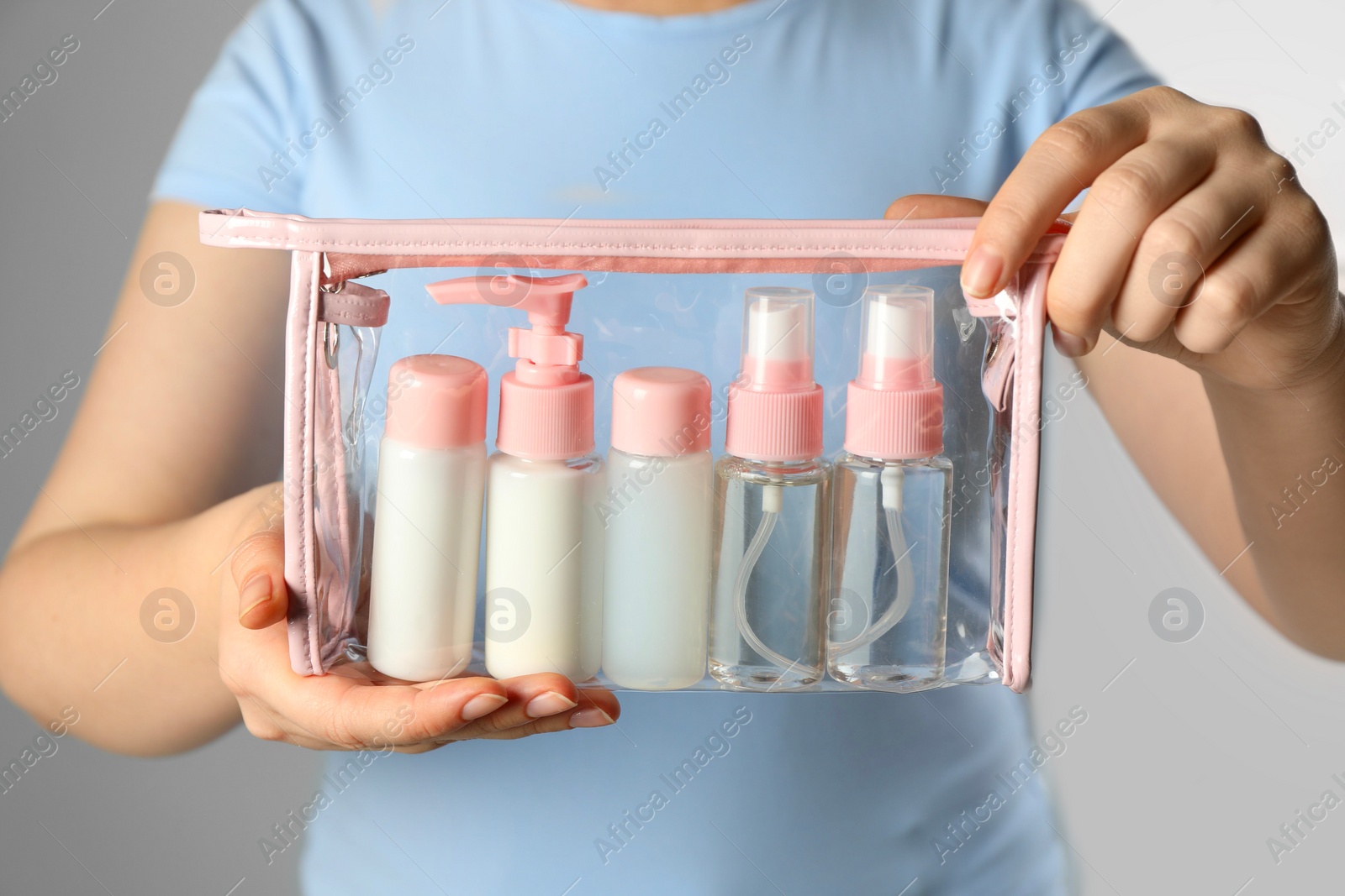 Photo of Woman with cosmetic travel kit on light background, closeup