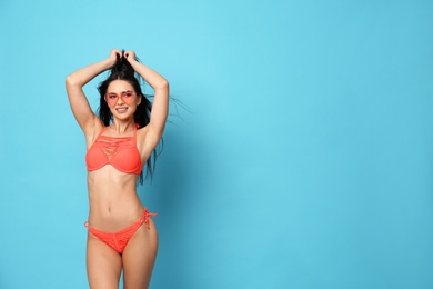 Beautiful young woman in stylish bikini with sunglasses on light blue background. Space for text