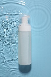 Photo of Bottle of face cleansing product in water against light blue background, top view