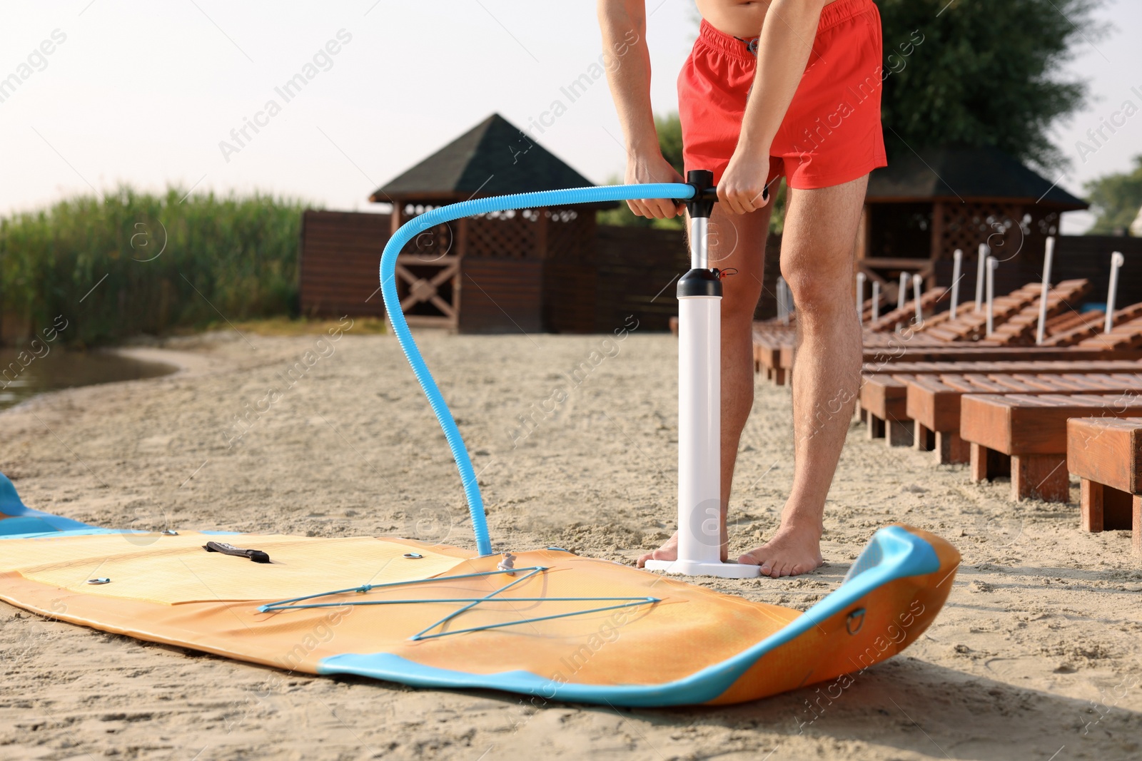 Photo of Man pumping up SUP board on river shore, closeup