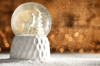 Snow globe with deer and trees on wooden table against festive lights, space for text. Christmas season