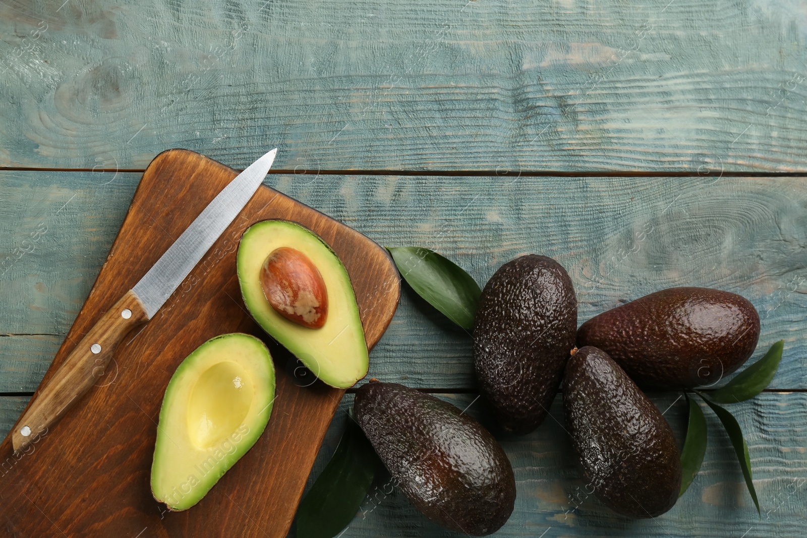 Photo of Whole and cut ripe avocadoes with leaves on light blue wooden table, flat lay