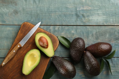 Photo of Whole and cut ripe avocadoes with leaves on light blue wooden table, flat lay