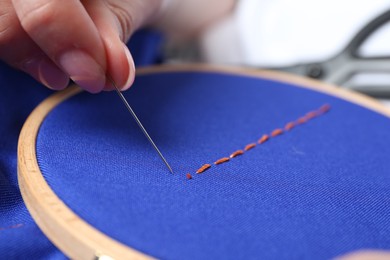 Woman with sewing needle and thread embroidering on cloth, closeup