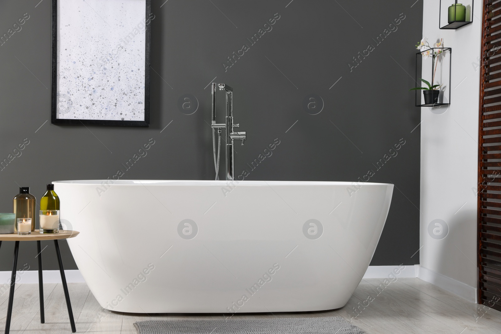 Photo of Stylish bathroom interior with ceramic tub and care products on coffee table