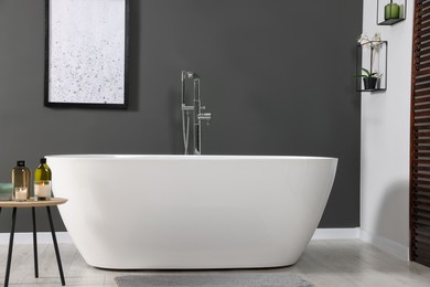 Stylish bathroom interior with ceramic tub and care products on coffee table