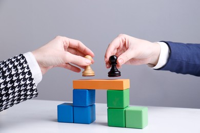 Photo of Businesspeople putting pawns on bridge made of colorful blocks at table, closeup. Connection, relationships and deal concept