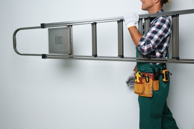 Photo of Professional builder carrying metal ladder on light background, closeup