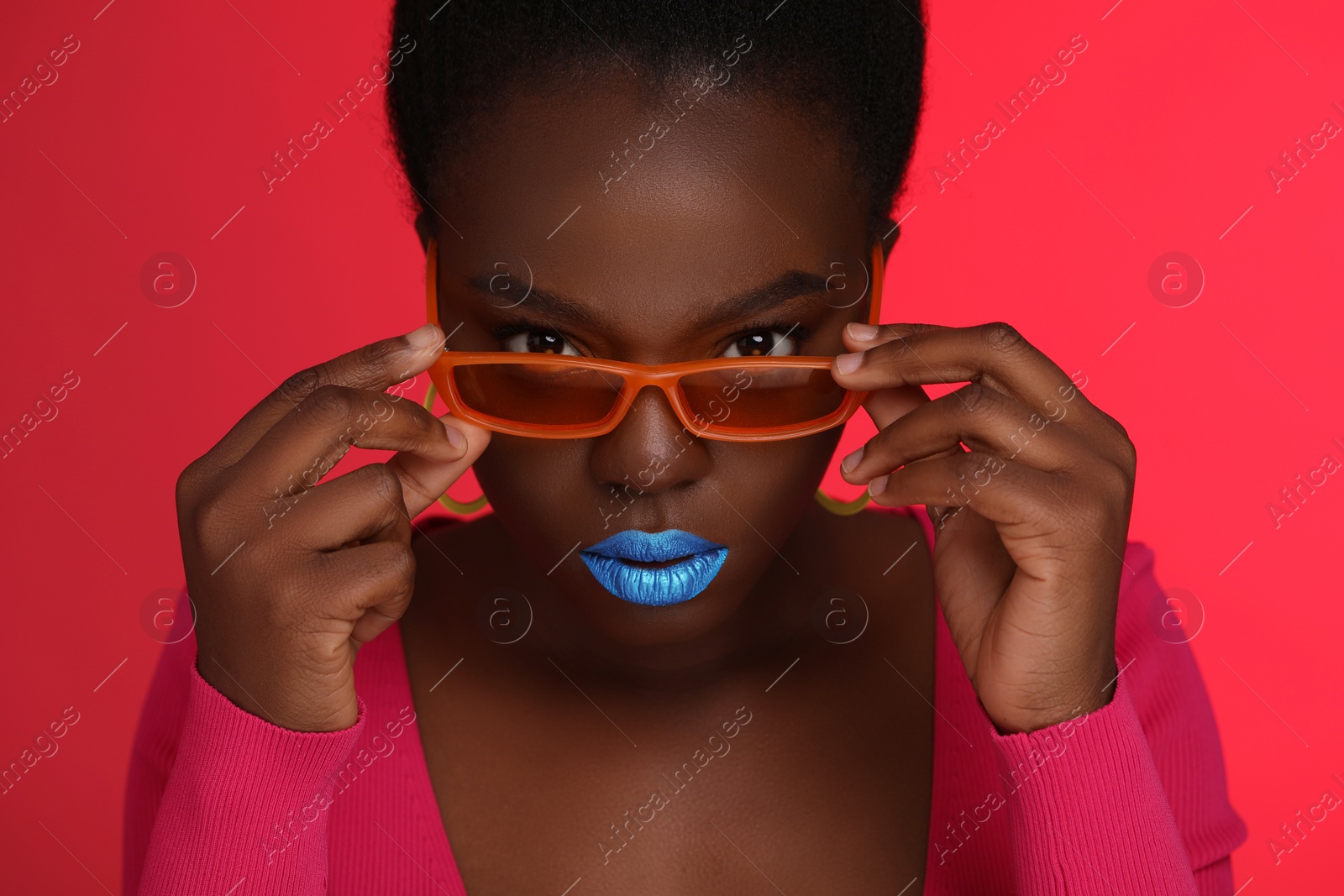 Photo of Fashionable portrait of beautiful woman with stylish sunglasses on coral background, closeup