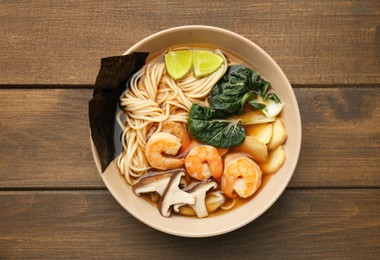 Photo of Delicious ramen with shrimps and mushrooms in bowl on wooden table, top view. Noodle soup