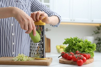 Photo of Woman grating zucchini at kitchen table, closeup