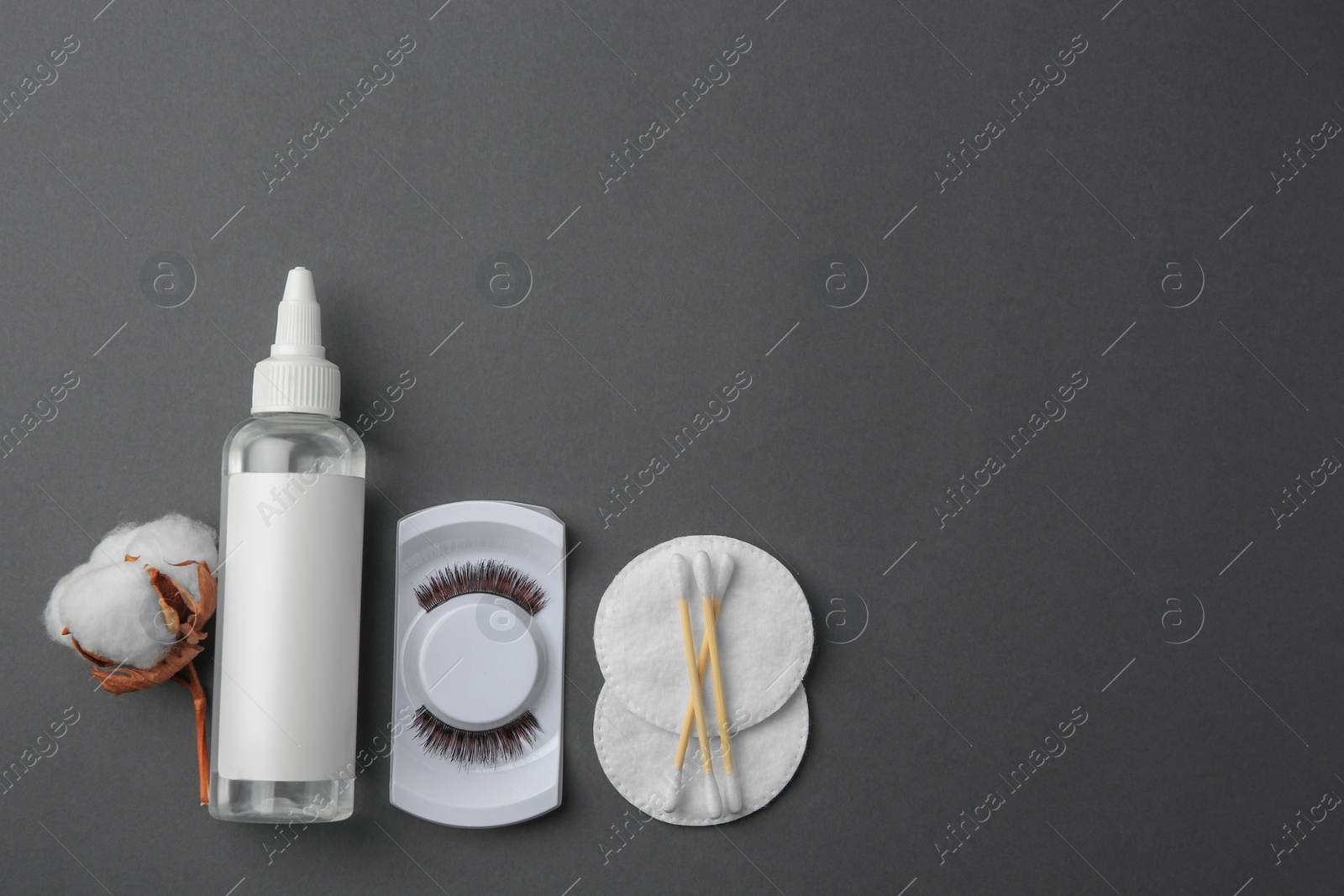 Photo of Bottle of makeup remover, cotton flower, pads, swabs and false eyelashes on grey background, flat lay. Space for text
