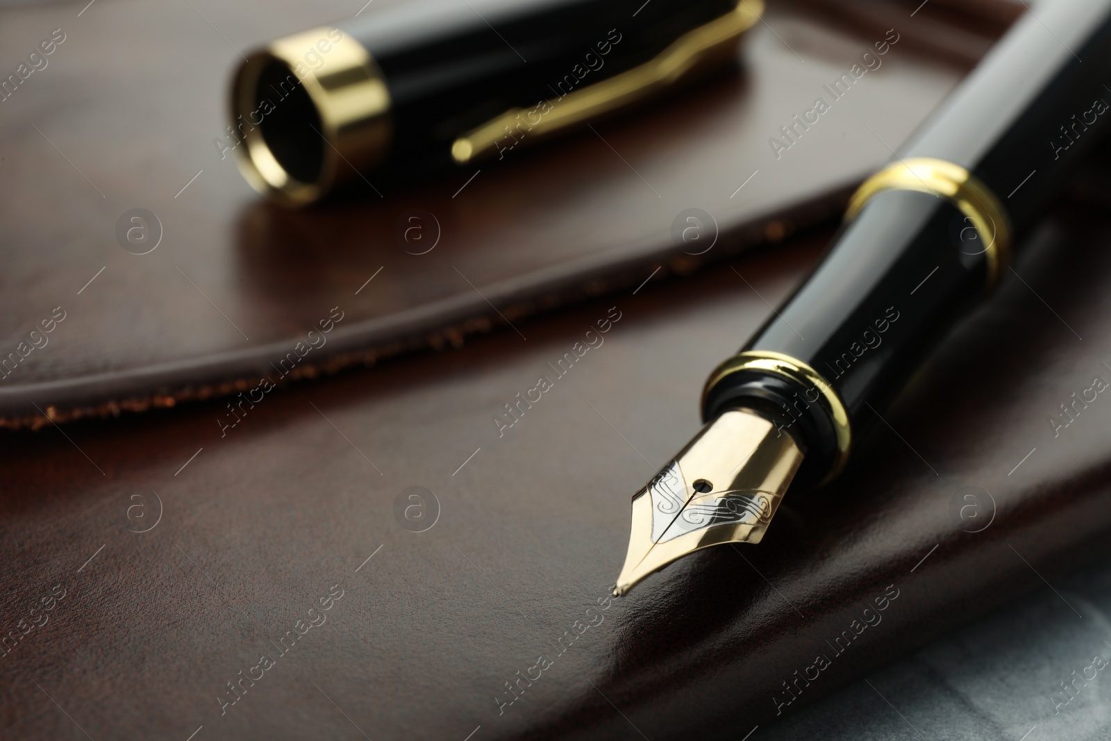 Photo of Stylish fountain pen, cap and leather notebook on grey table, closeup