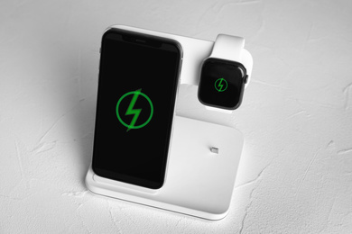 Photo of Mobile phone and smartwatch charging with wireless pad on white stone table
