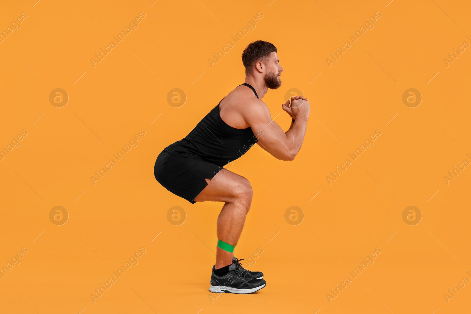 Photo of Young man exercising with elastic resistance band on orange background