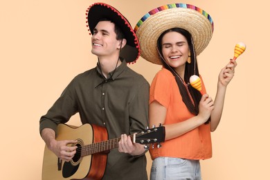 Photo of Lovely couple woman in Mexican sombrero hats with maracas and guitar on beige background