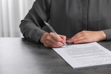 Photo of Woman signing document at dark table indoors, closeup