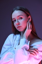 Fashionable portrait of beautiful young woman on purple background in neon lights