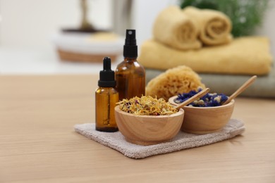 Photo of Bottles of essential oils, bowls with dry flowers and natural sponge on light wooden table, space for text. Spa therapy