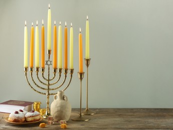 Photo of Composition with Hanukkah menorah, dreidels and donuts on wooden table against light background. Space for text