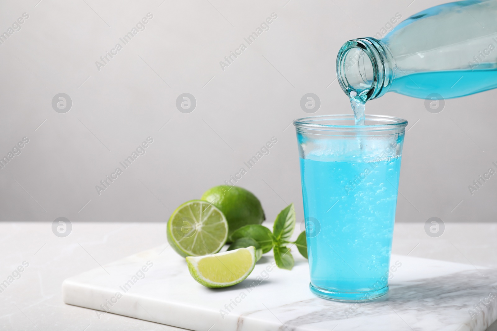 Photo of Pouring refreshing light blue drink into glass on white table, space for text