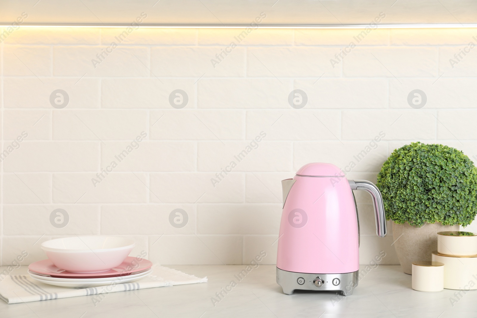 Photo of Modern electric kettle, dishes and houseplant on counter in kitchen