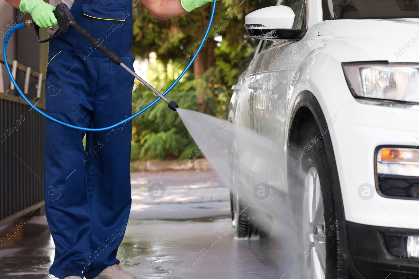 Photo of Worker washing auto with high pressure water jet at outdoor car wash, closeup