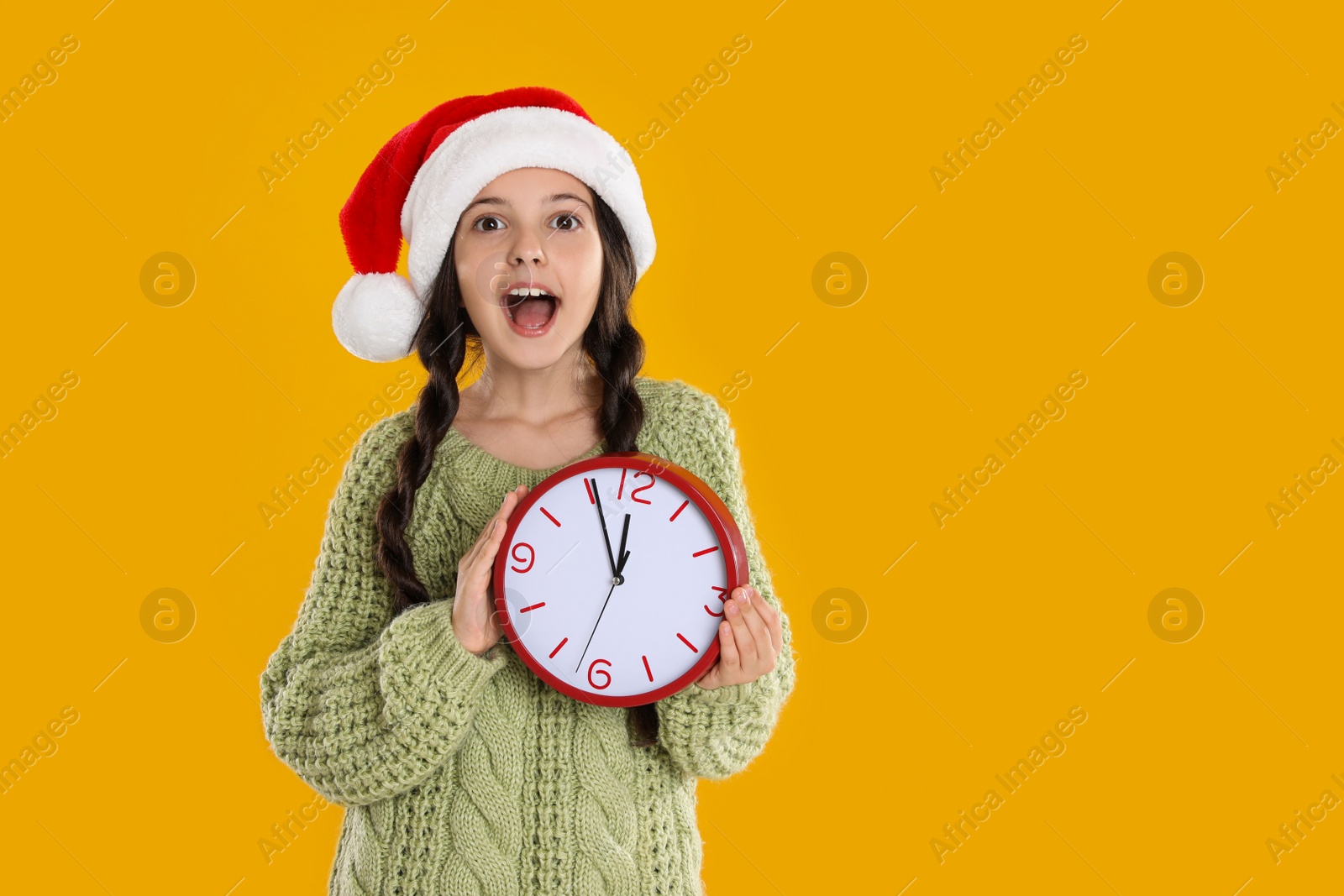 Photo of Girl in Santa hat with clock on yellow background, space for text. New Year countdown