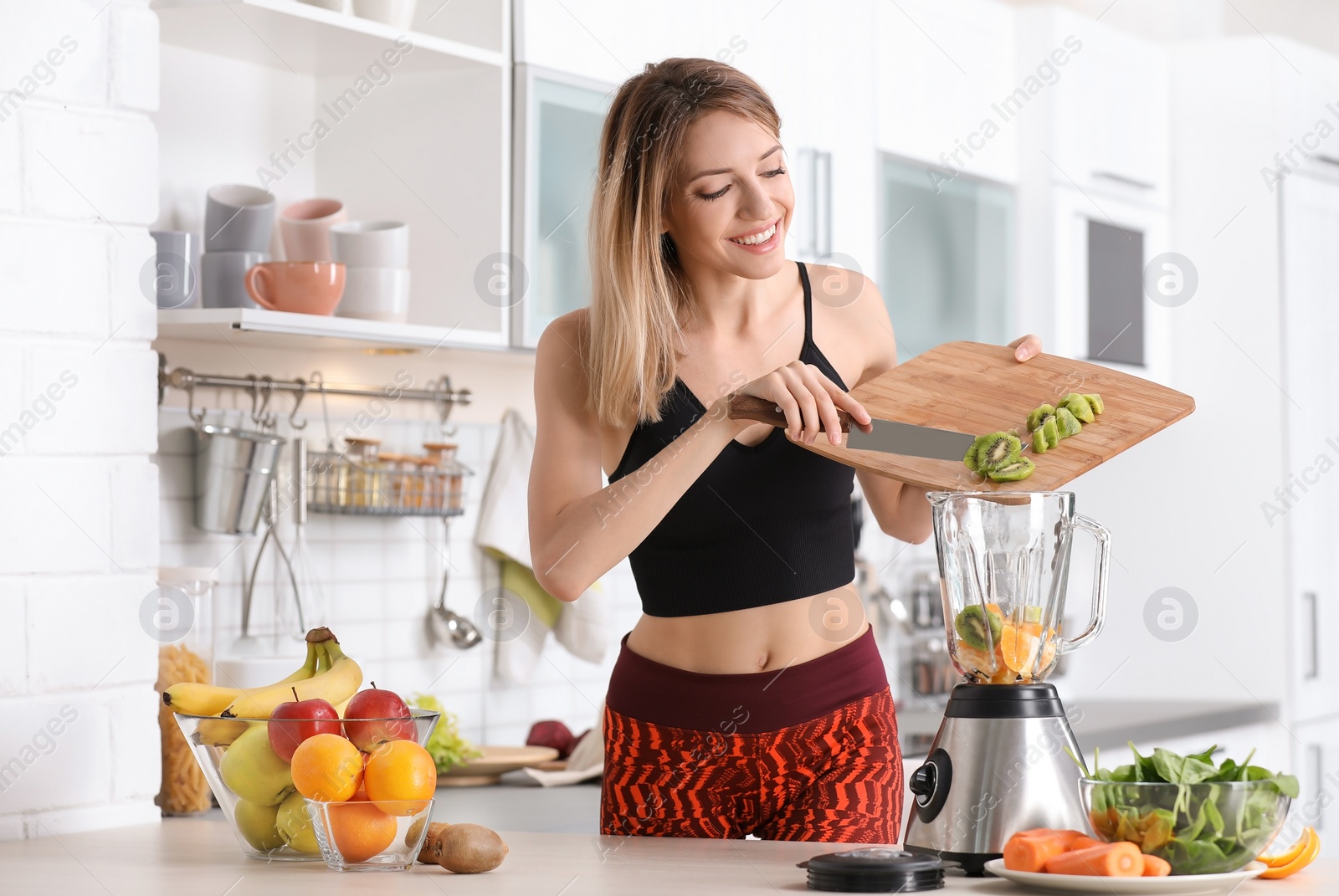 Photo of Young woman preparing tasty healthy smoothie at table in kitchen