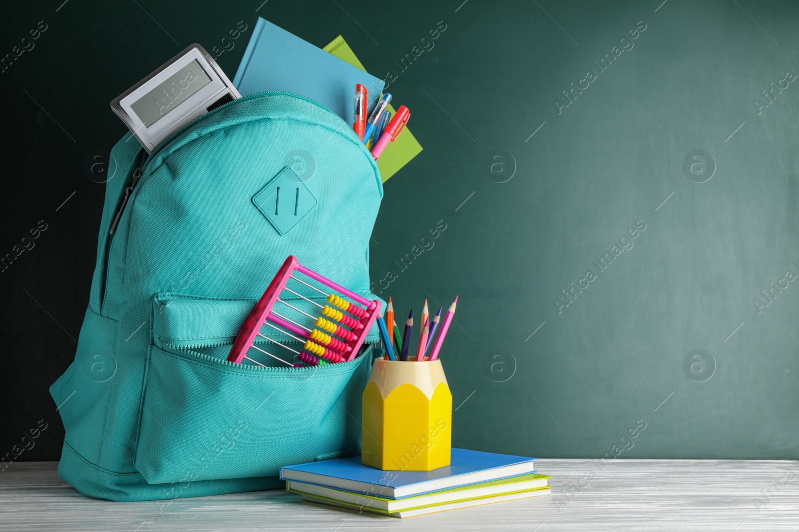Photo of Stylish backpack with different school stationary on white wooden table at green chalkboard. Space for text