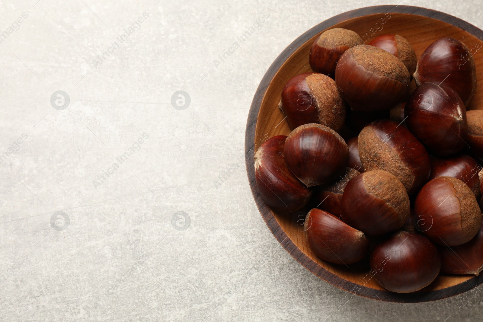 Photo of Roasted edible sweet chestnuts in bowl on light grey table, top view. Space for text