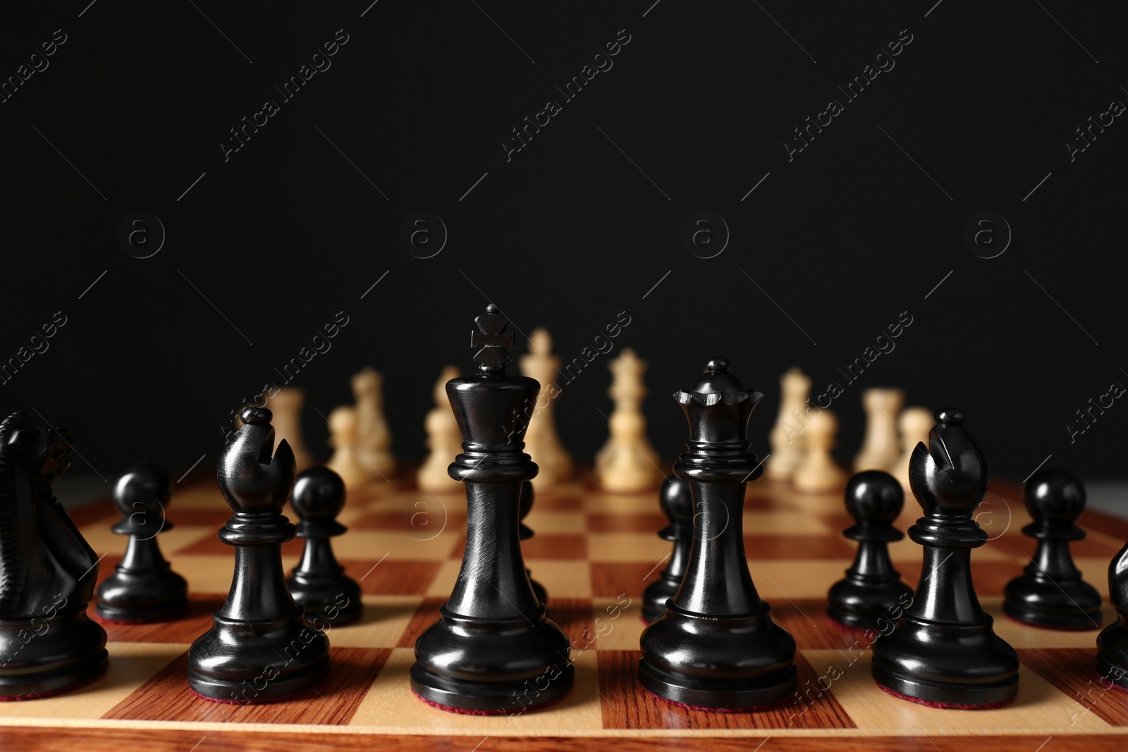 Photo of Chess pieces on wooden board against black background