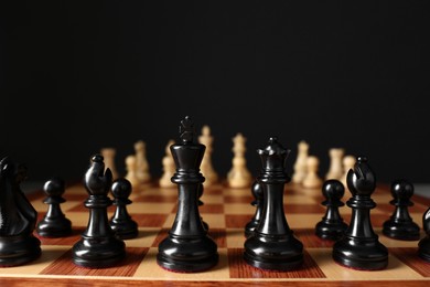 Chess pieces on wooden board against black background