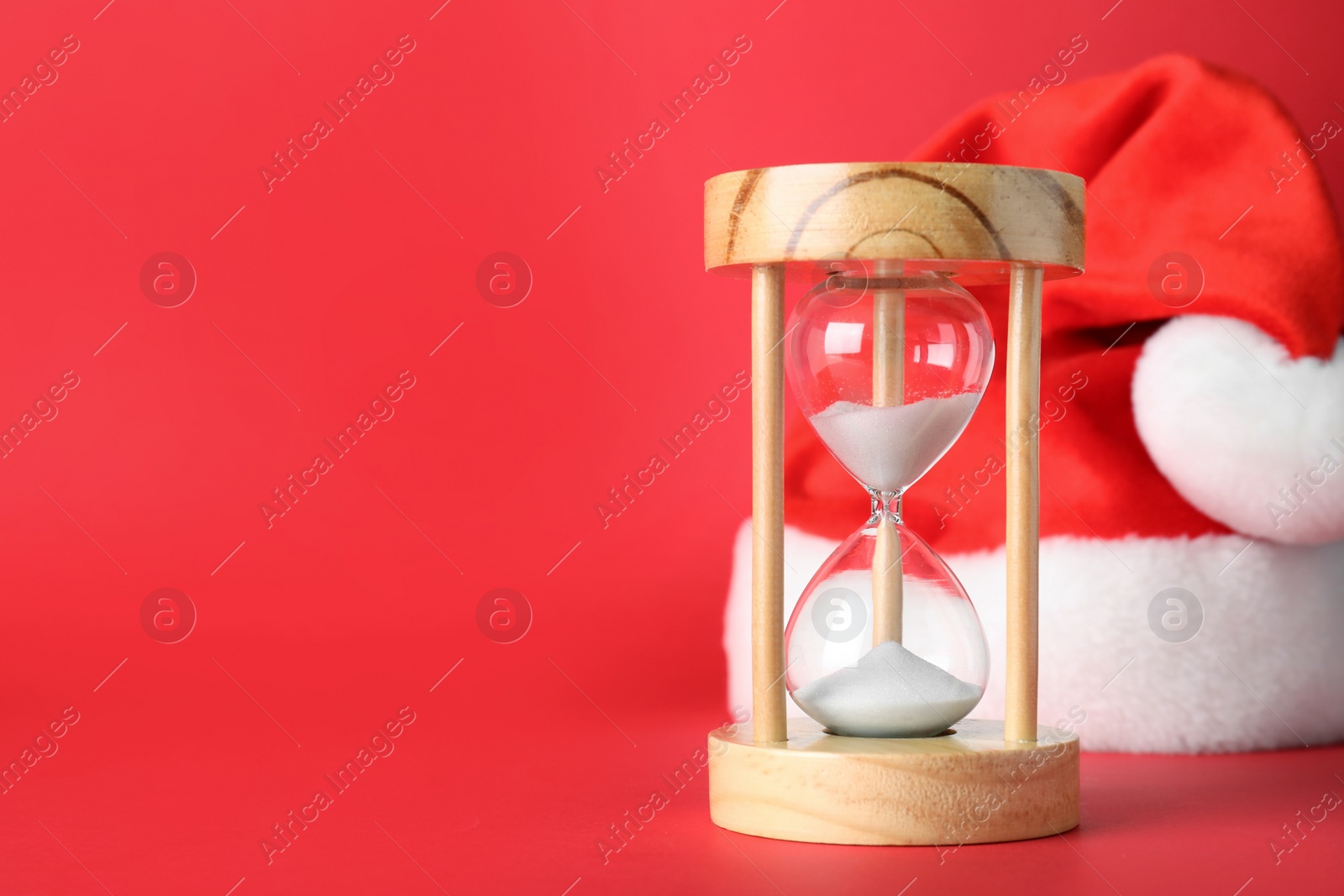 Photo of Hourglass and Santa hat on red background, space for text. Christmas countdown