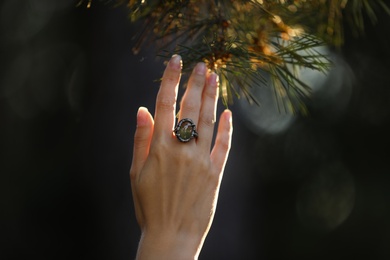 Young woman wearing beautiful silver ring with prehnite gemstone near pine, closeup