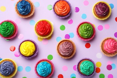 Photo of Many delicious colorful cupcakes and confetti on violet background, flat lay