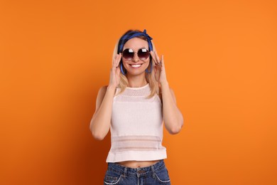 Photo of Portrait of smiling hippie woman in sunglasses on orange background
