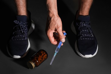 Man taking syringe from black floor, closeup. Doping concept