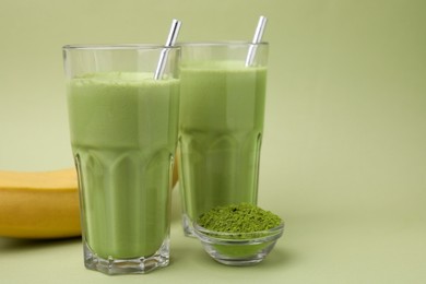 Photo of Glasses of tasty matcha smoothie and powder on pale green background. Space for text