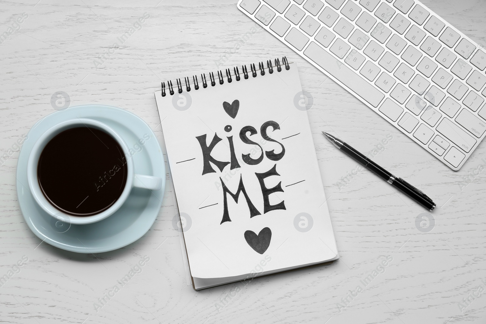 Notebook with phrase Kiss Me, keyboard, cup of drink and pen on white wooden table, flat lay Photo of Notebook with phrase Kiss Me, keyboard, cup of drink and pen on white wooden table, flat lay