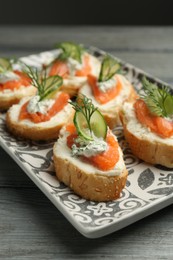 Tasty canapes with salmon, cucumber, cream cheese and dill on wooden table, closeup