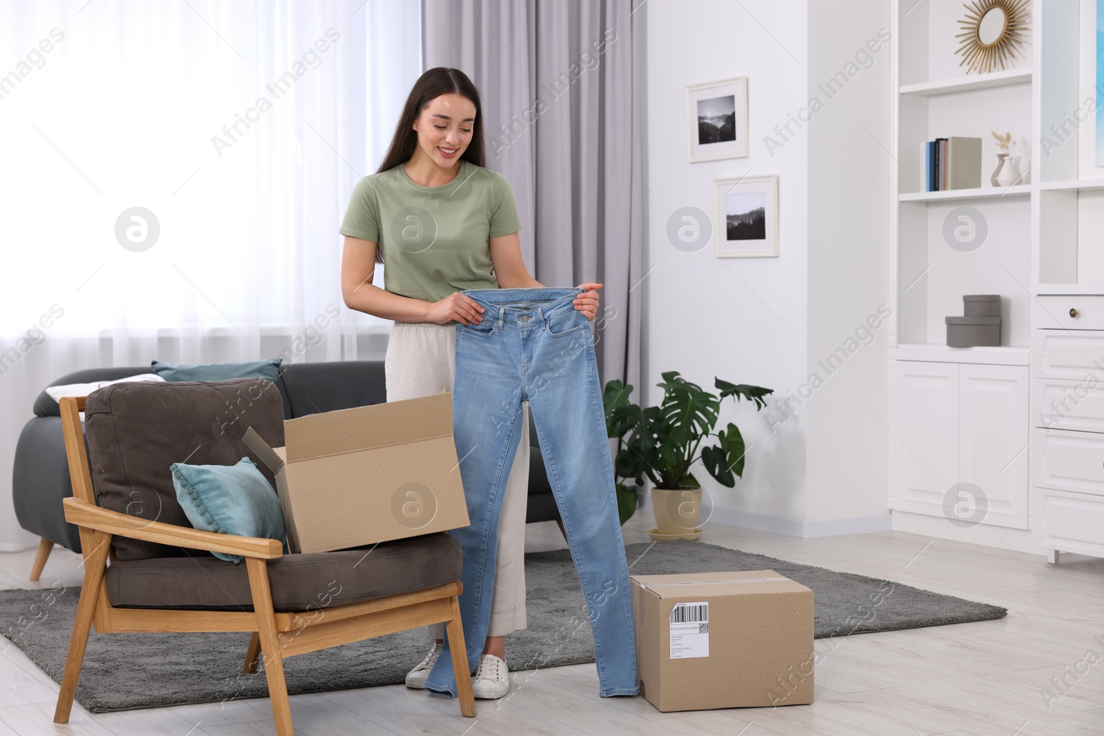 Photo of Happy woman with stylish light blue jeans at home. Online shopping