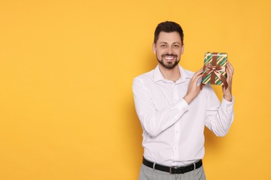 Photo of Happy man with gift box on yellow background, space for text