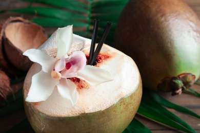 Fresh green coconut with drinking straws and orchid flower on table, closeup