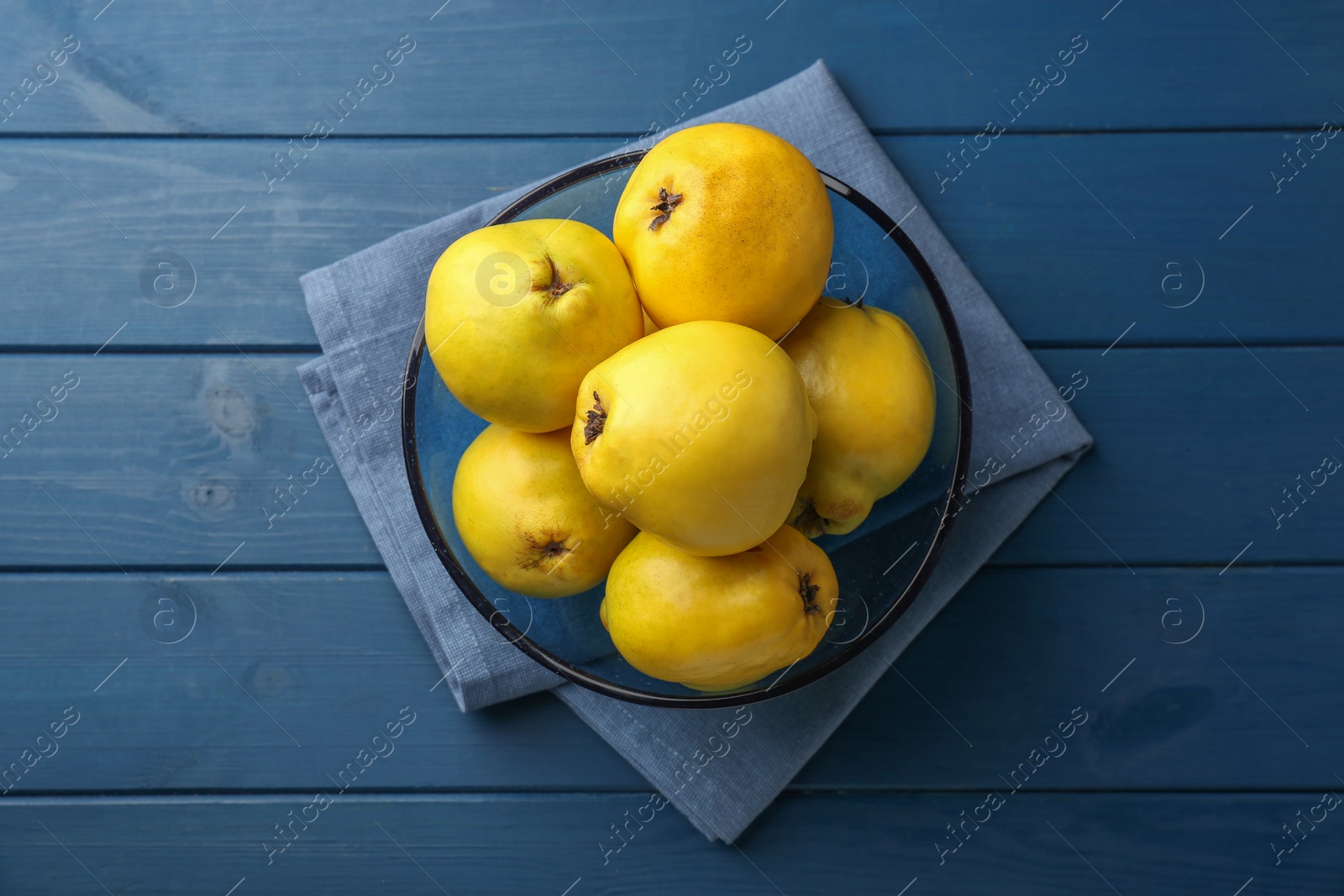 Photo of Tasty ripe quinces in bowl on blue wooden table, top view