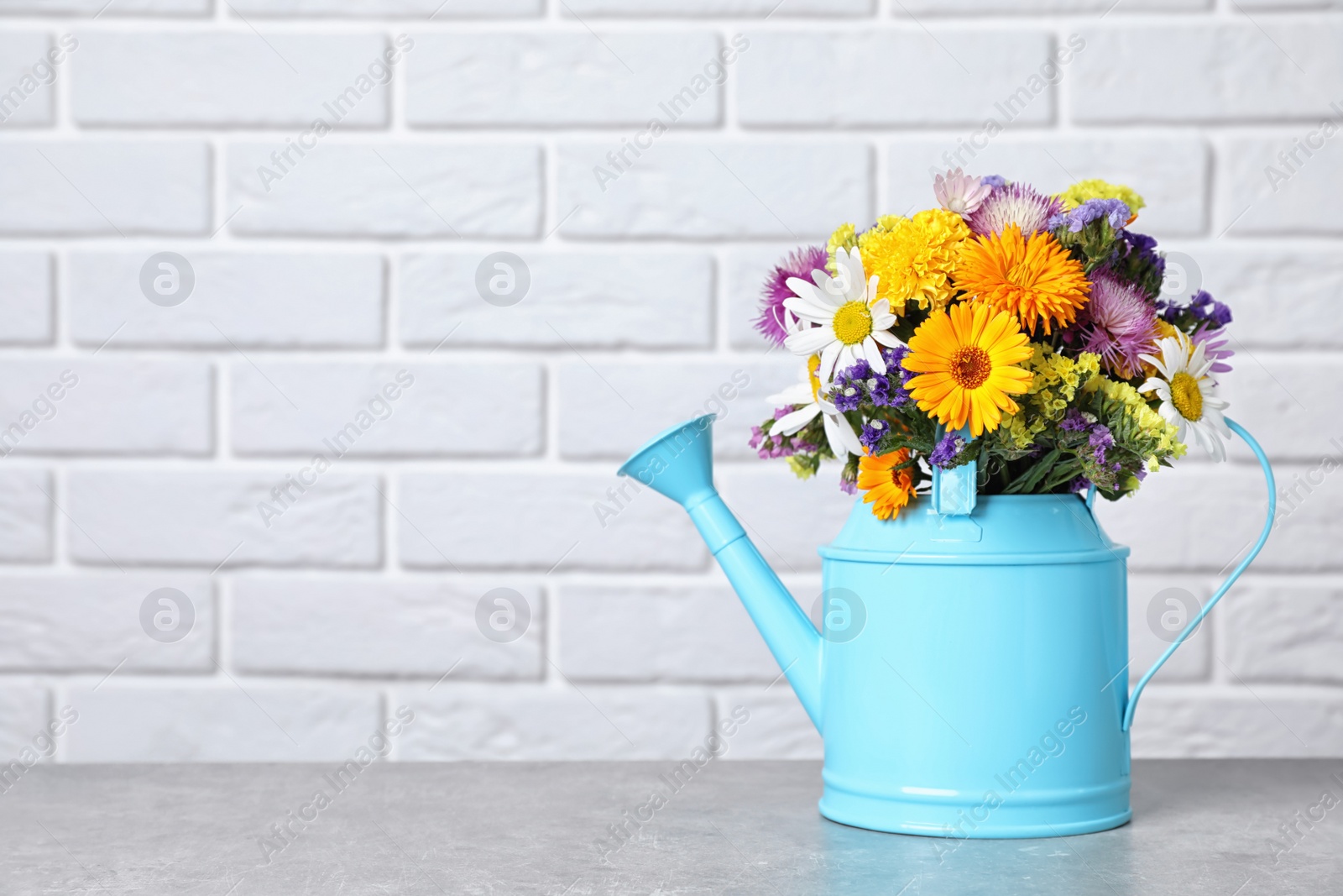 Photo of Watering can with beautiful wild flowers on table near brick wall