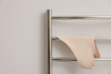 Photo of Heated towel rail with beige underwear on white wall, closeup. Space for text